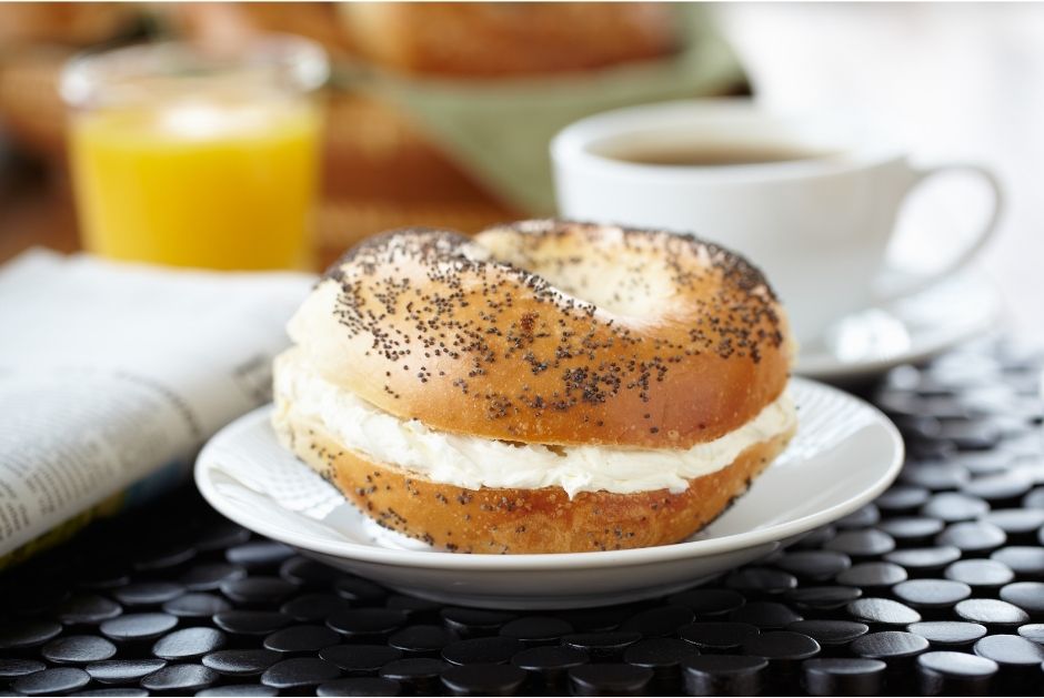 Bagel with cream cheese spread with orange juice and coffee in background