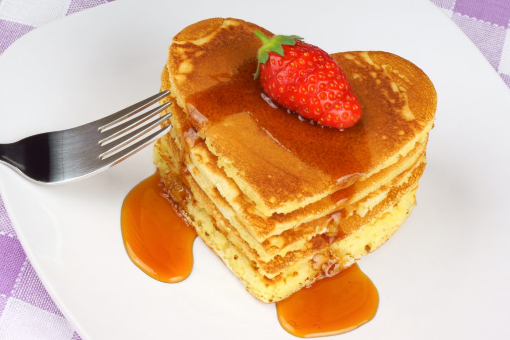 Heart-shaped pancakes with syrup and a strawberry on a white dish. A perfect breakfast for Valentine's Day.