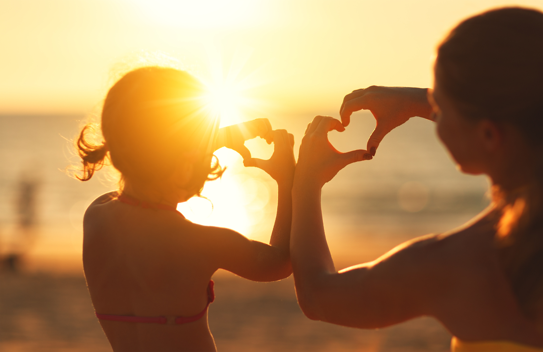 The concept of love, parenthood and a happy family. Mother and child daughter show heart from hands at sunset on beach