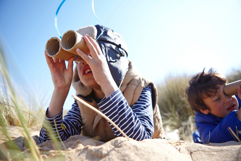 two young kids with homemade binoculars looking for birds while laying on the beach
