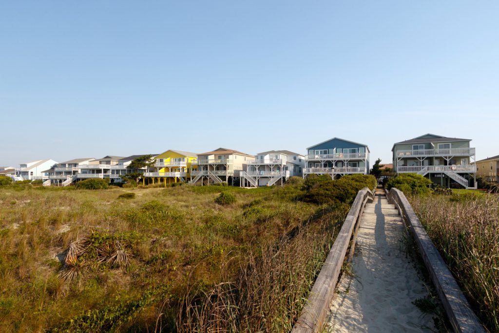 Beach houses across the green sand dunes with a long wooden walkway, Holden Beach, North Carolina